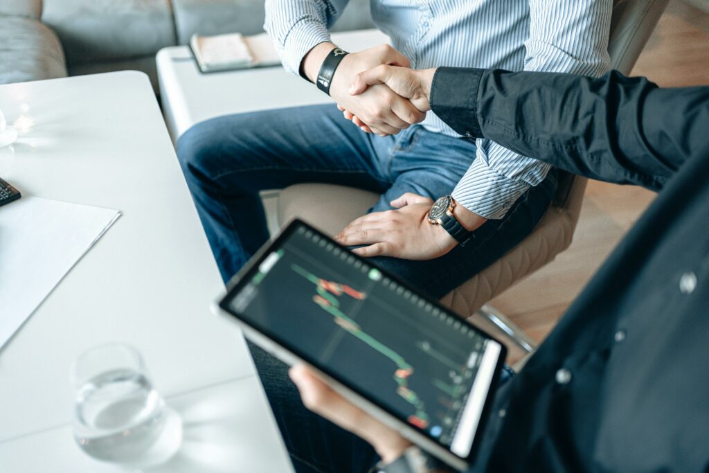 Two people shaking hands over a table with data on a tablet, representing trusted relationships